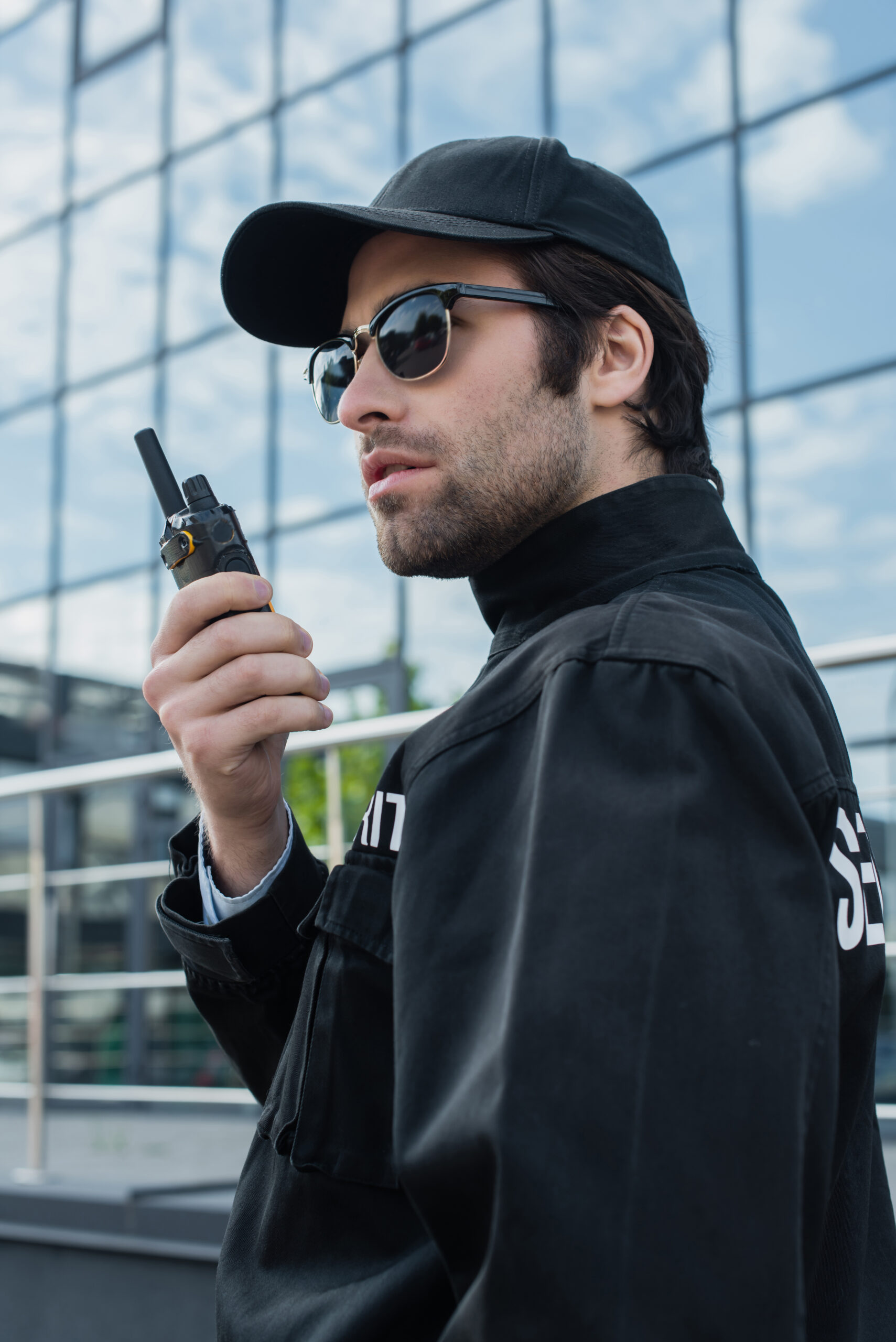 serious guard in sunglasses and black uniform talking on radio set outdoors About Metrotalk